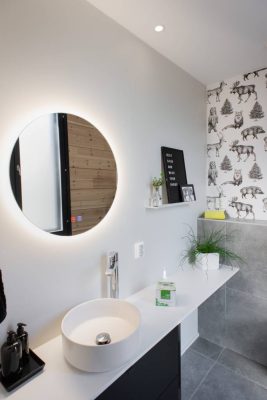 Toalettbelysning-MOON-led-lighting-with-mirror-second-9W-Led-Pyorea-spoteilla_ledstorefi- - LedStore Nykyaikainen kylpyhuone LedStore.fi:n led-valaistuksella: Pyöreä, taustavalaistu LED-peili koristaa valkoisen altaan yläpuolella, jossa on korkea hana. Eläinaiheinen tapetti tuo persoonallisuutta seiniin. Musta kirjetaulu ja pieni viherkasvi täydentävät tunnelman hyllyllä, kun taas harmaat laatat lattialla luovat tyylikkään ilmeen.