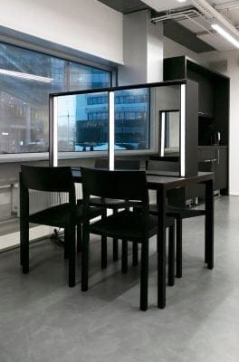 Moderni toimistotila, johon kuuluu pöytä ja neljä mustaa tuolia, voi nyt saada uuden ilmeen LedStore.fi:n tarjoamalla valaistusratkaisulla. Pöydän väliseinä peileineen tuo tilaan modernia ilmettä, kun taas energiaa säästävä LED-valaistus täydentää minimalista designia loistavasti. Suuret ikkunat avautuvat näkymään kadun toisella puolella sijaitsevaan rakennukseen, ja tyylikäs harmaa lattia korostaa kokonaisuuden nykyaikaista tunnelmaa. Använd LED-valikoimaamme och valits sopiva ratkaisu juuri sinun tilaasi!