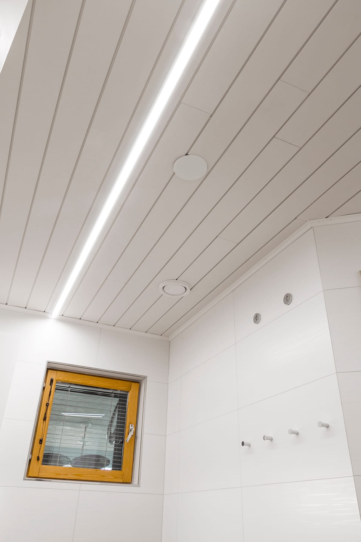 IMG_7745 kopio - LedStore Näköala moderniin huoneen katosta, jossa on valkoiset paneelit ja upotetut LED-valaisimet LedStore.fi:n valikoimasta. Huoneen vasenta seinää koristaa pieni puukehyinen ikkuna, kun taas oikeastasta kohoavat siitä valkoiset koukut. Kolmen pyöreää LED-valaisinta ovat elegantisti oikeana kattoon.
