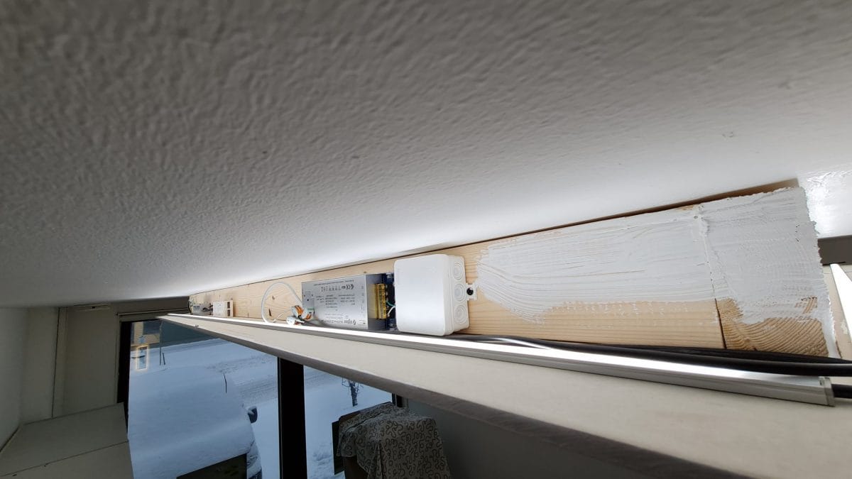 Lähikuva kattopalkista esittelee LED-valaistuja sähkökomponentteja, kun osittain valkoiseksi maalattu puu luo moderniin ilmeen. Taustalla ikkunasta avautuu näkymä lumiseen maisemaan, mikä tuo tilaan raikasta luonnonvaloa. Tutustu LedStore.fi:n korkealaatuisiin LED-valaisimiin luodaksesi oman tunnelmallisen valaistuskokonaisuutesi.
