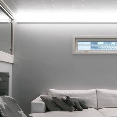 Un soggiorno minimalista con luce naturale, tende alla finestra e luci LED soffuse su pareti grigie.