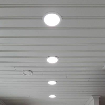 Quattro plafoniere LED da incasso illuminano una stanza rivestita di bianco. I pannelli LED rotondi illuminano con un ampio fascio di luce.