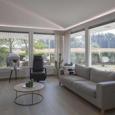 Soggiorno moderno con plafoniere a LED, lampada da terra, luce naturale da ampie finestre, comode sedute.