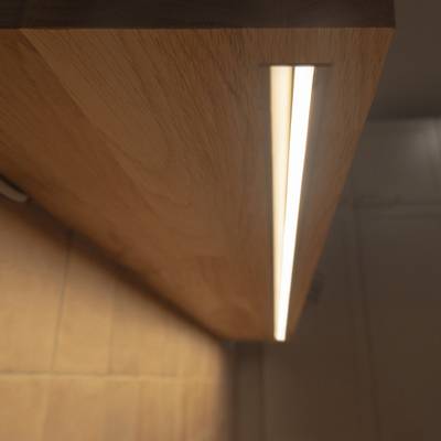 La striscia LED posizionata sotto la mensola in legno proietta sulla parete una luce indiretta e calda, ideale come illuminazione d'accento