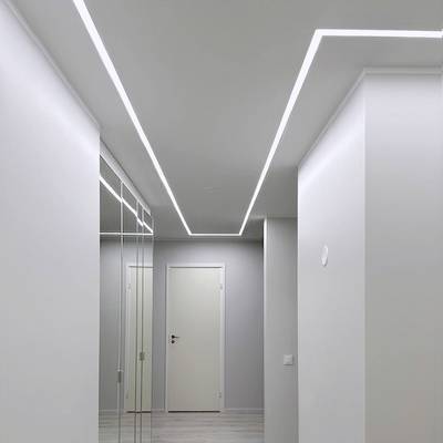 Corridoio moderno con pareti bianche, porta chiusa, mobile a specchio e plafoniere a incasso con motivo geometrico.