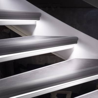 Una vista dettagliata di una scala galleggiante con un elegante apparecchio di illuminazione a LED, un'illuminazione d'accento e una parete bianca.