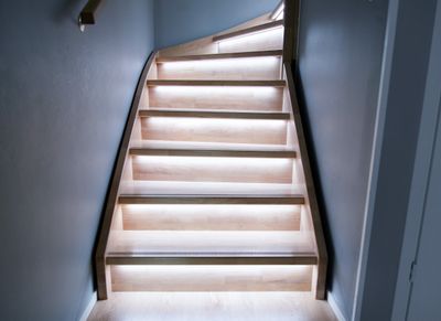 Una moderna scala in legno con luci LED sotto ogni gradino, che mette in risalto il design minimalista con una luce calda sulle pareti grigie.