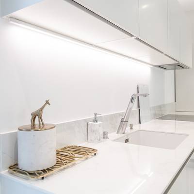 Cucina moderna con piano di lavoro bianco, rubinetto argentato, figura di giraffa nella vasca; illuminazione LED luminosa sotto gli armadietti per aumentare lo spazio.