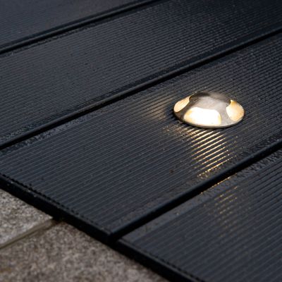 Lampada da ponte rotonda di colore argento con pannelli di legno scuri e scanalati, che emette una luce soffusa di notte. Ideale per soluzioni di illuminazione a LED per esterni.