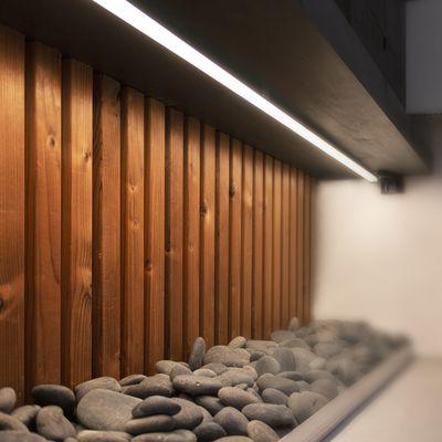 Moderna parete rivestita in legno con pietre di fiume nere e un'elegante luce LED lineare al di sopra. Illuminazione LED elegante ed efficiente per la decorazione della casa.