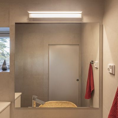 Bagno moderno con illuminazione a LED a risparmio energetico, ampio specchio, piano d'appoggio beige, rubinetto elegante e gancio per asciugamani rosso per un interno elegante.