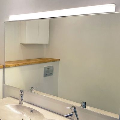 Bagno con specchio illuminato a LED, lavabo e rubinetteria moderni, mensola in legno e mobiletti bianchi. La soluzione di illuminazione ideale del negozio di illuminazione a LED.