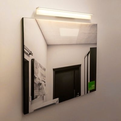 Testo alternativo: un corridoio moderno con pareti bianche, una porta scura e un apparecchio LED che si riflette su uno specchio crea un'atmosfera di illuminazione LED contemporanea.