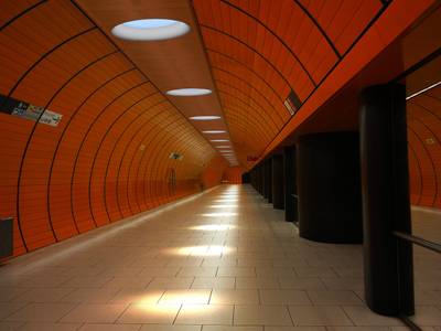 Lumini a LED luminosi illuminano un moderno tunnel della metropolitana, le cui pareti sono di colore arancione e il pavimento è piastrellato.