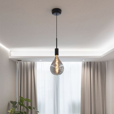 Una lampada a sospensione con lampadina Edison e lampada nera illumina la stanza con tende leggere e crea un'atmosfera calda.