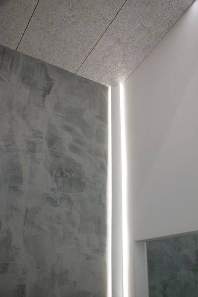 Una parete grigia strutturata incontra una parete bianca liscia con una striscia luminosa a LED verticale.