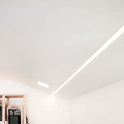 Una stanza moderna con soffitto inclinato, un'elegante illuminazione lineare LED a incasso e scaffali angolari con diversi prodotti decorativi.