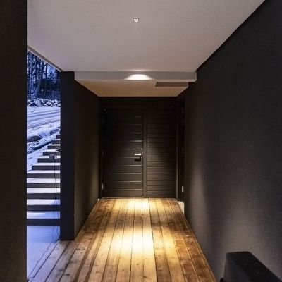 Testo alternativo: ingresso moderno con pareti scure, pavimento e scala in legno illuminati a LED; porta nera che conduce all'esterno innevato. Atmosfera perfetta per interni eleganti.