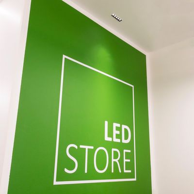Testo alternativo: 'Parete verde con profilo quadrato bianco 'LED STORE', lettere in grassetto, luci a soffitto'