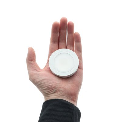 Piccolo apparecchio LED rotondo a mano sotto un mobile con base bianca.