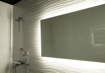 Il bagno moderno è caratterizzato da piastrelle bianche, un grande specchio retroilluminato e un elegante soffione e rubinetto argentati con un'elegante illuminazione a LED.