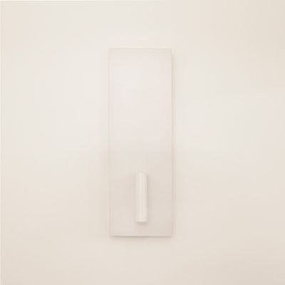 Scultura minimalista da parete bianca con base rettangolare e proiezione cilindrica centrale, illuminata da una luce a LED che aumenta l'attrattiva del design.