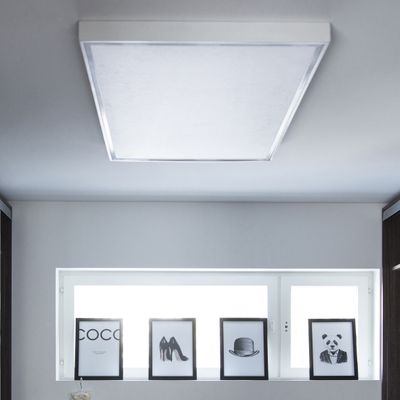 Una luce LED a soffitto illumina immagini monocromatiche incorniciate di testi, scarpe, cappelli e panda su una mensola accanto a una finestra in un interno di casa moderna.