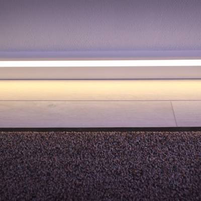 Una moderna striscia LED illumina il passaggio tra la moquette e il pavimento in legno, mettendo in risalto i dettagli bianchi del battiscopa.