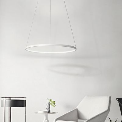 Un interno minimalista con una moderna lampada a sospensione circolare a LED, una sedia e un tavolo bianchi e una piccola pianta in vaso per creare un'atmosfera tranquilla.