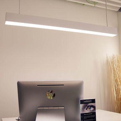 Elegante lampada da tavolo a LED che illumina un ufficio moderno con un computer su una scrivania bianca; sullo sfondo rami decorativi in un vaso alto.