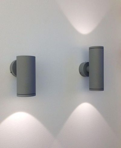 Le moderne applique cilindriche a LED proiettano una luce morbida verso l'alto e verso il basso su una parete bianca, creando un ambiente elegante in un design di illuminazione contemporaneo.