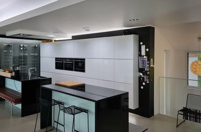 Cucina moderna con armadietti bianchi, isola nera, elettrodomestici da incasso e illuminazione a LED sulla zona giorno.