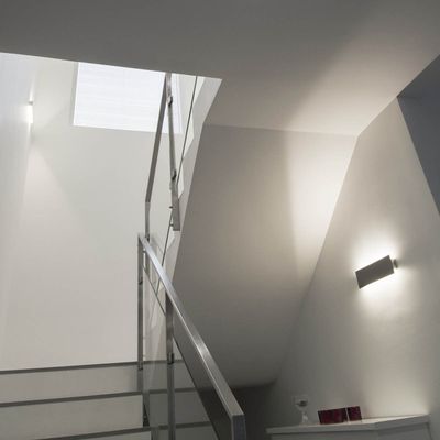 Scala moderna con ringhiera in metallo, pareti grigie e illuminazione a parete a LED che conduce a una piccola finestra sovrastante - illuminazione a risparmio energetico.