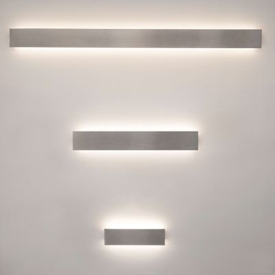 Tre apparecchi LED rettangolari e verticali che irradiano una luce calda su una parete chiara; ideali per soluzioni di illuminazione domestica moderna.