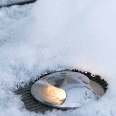 Testo alternativo: 'Lampada da terra parzialmente innevata che crea un caldo bagliore nel paesaggio invernale - una vetrina di prodotti per l'azienda di illuminazione a LED.