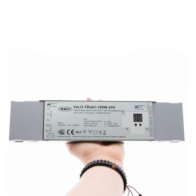 Primo piano di una mano che tiene in mano il dimmer LED VaLO TRIAC-100W-24V con display digitale, che migliora l'efficienza energetica dell'illuminazione a LED.