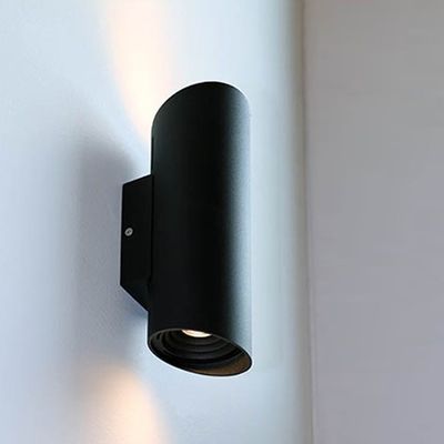 Moderna applique cilindrica nera con parete bianca, la luce LED bidirezionale irradia verso l'alto e verso il basso per un'illuminazione elegante.