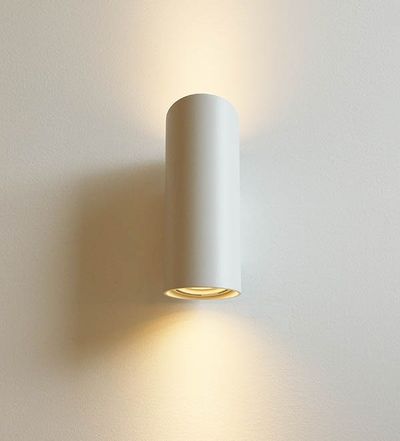 Un'elegante applique LED cilindrica illumina fasci di luce calda su e giù per una parete bianca; ideale per interni moderni e minimalisti.
