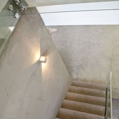 Una scala moderna con gradini in cemento, balaustra in vetro e luce LED a parete che risplende in modo caldo; il design minimalista aggiunge atmosfera all'ambiente.