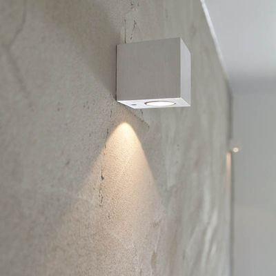Un moderno apparecchio LED quadrato da parete che illumina una parete beige testurizzata per soluzioni di illuminazione domestica eleganti ed efficienti dal punto di vista energetico.