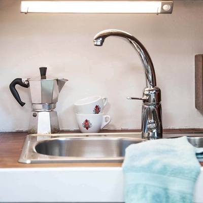 Moderno lavello da appoggio con rubinetto cromato, caffettiera moka, tazze sovrapposte con logo rosso, asciugamano azzurro sul bancone: il luogo perfetto per l'illuminazione LED a risparmio energetico.