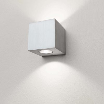 Testo alternativo: "Moderna applique LED quadrata con parete bianca strutturata, illumina dolcemente verso l'alto e verso il basso.