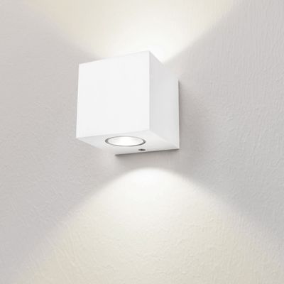 Un'applique minimalista a forma di cubo bianco illumina una parete bianca dalla texture morbida con luce verso l'alto e verso il basso. Perfetto per una moderna illuminazione a LED.