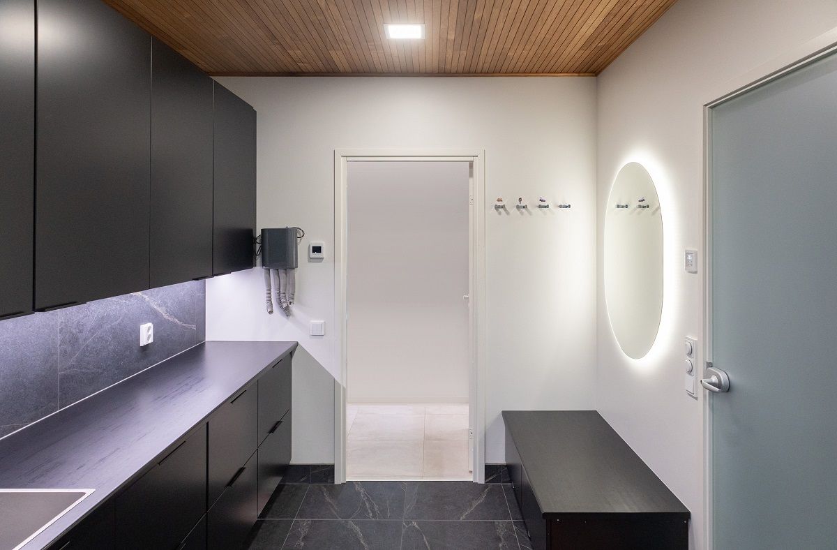 Nel soffitto di una stanza per la cura della casa, una piccola lampada a pannello rettangolare, uno specchio ovale e una striscia LED illuminano il piano di lavoro.