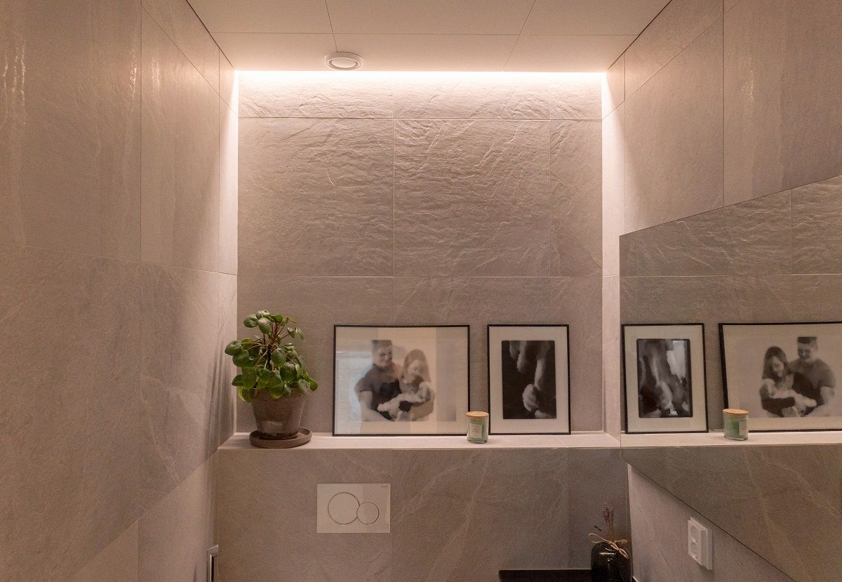 Striscia LED montata a filo tra parete e soffitto in una toilette.