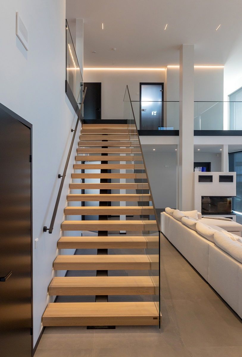 Scala in legno chiaro che porta al piano superiore illuminata da una striscia a led e una striscia a led che corre intorno alla parete del piano superiore