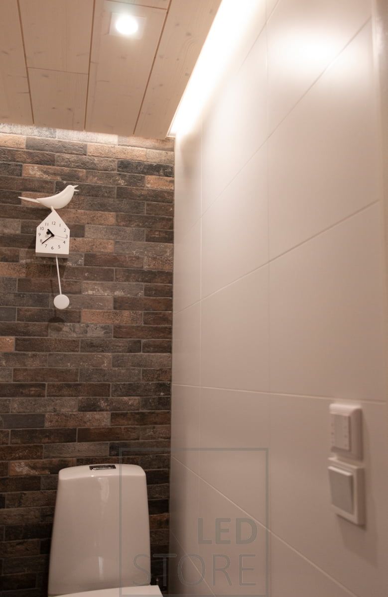 Illuminazione con downlight LED - LIGHT GREEN R023 e illuminazione indiretta con profilo superficiale bianco nella scanalatura del soffitto con striscia da 7,2 W/m CCT. Un controller wireless montato sopra l'interruttore della luce è visibile anche sulla parete.