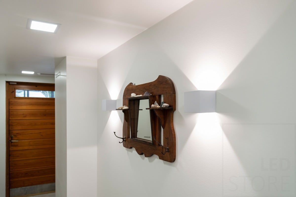 Logo LED STORE: testo bianco su sfondo verde con la scritta "LED" STORE in alto. Il quadrato bianco si trova in un negozio di illuminazione ecologica.