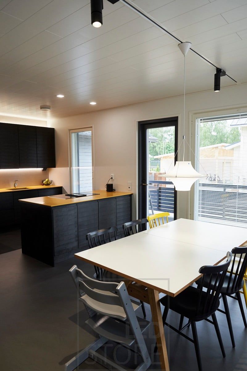 Illuminazione a binario nella sala da pranzo. In cucina, l'illuminazione indiretta sopra i mobili e l'illuminazione del piano di lavoro alla base dei mobili superiori illuminano lo spazio intermedio. Ledstore.fi