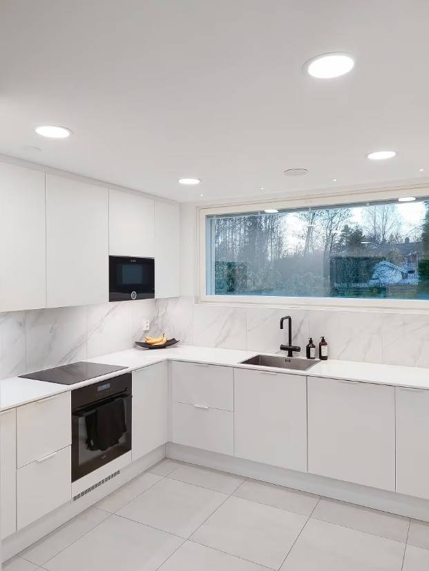 Luci a pannello sul soffitto della cucina, strisce LED sul lato inferiore degli armadi e piccoli punti luce d'accento allineati davanti alla finestra.  